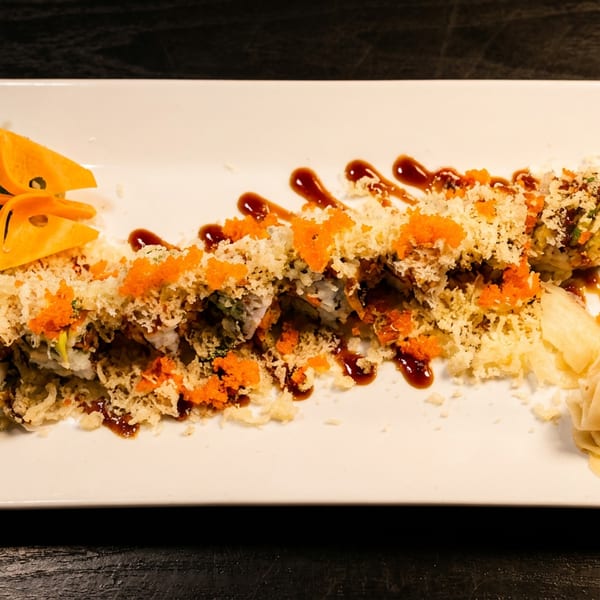 Sushi roll topped with crispy tempura flakes, orange tobiko, and eel sauce, served with ginger and wasabi.