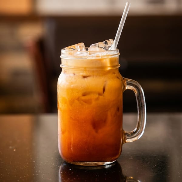 Iced Thai tea in a mason jar with a straw on a dark speckled table.