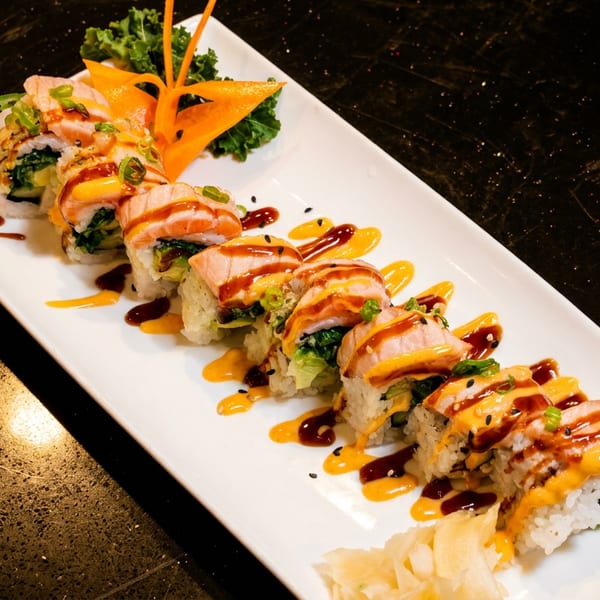 Sushi roll with salmon, green onions, and two sauces on a white rectangular plate.
